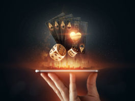 Top 10 Picks for the Best Online Casino: Reviews & Insights A hand holding a smartphone horizontally, from which glowing golden playing cards and dice are digitally emerging, symbolizing online gambling and casino entertainment. The background is dark with a subtle illuminated cityscape silhouette, enhancing the futuristic and dynamic feel of the image.